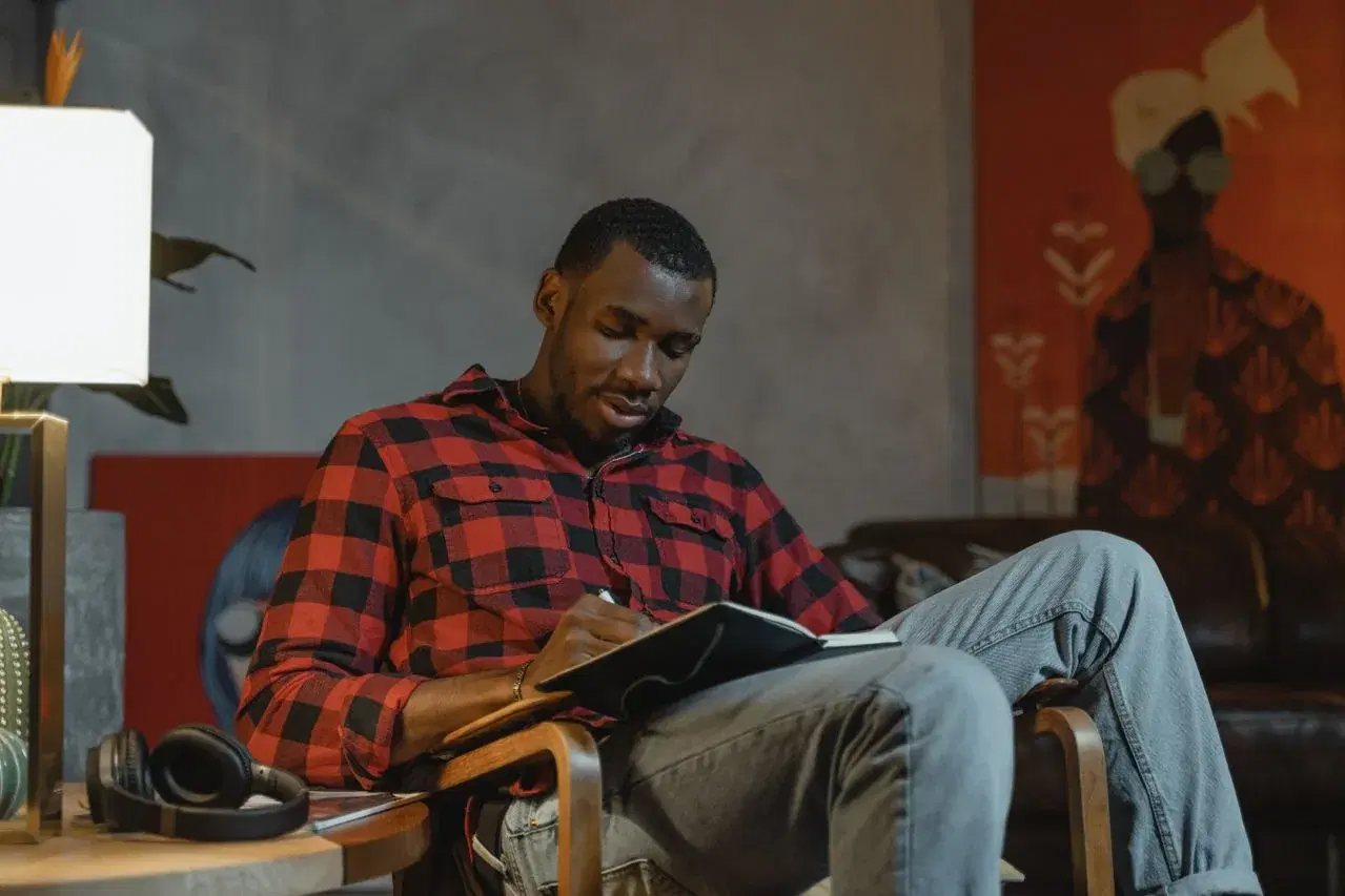 A man sitting alone in an armchair, writing in a journal