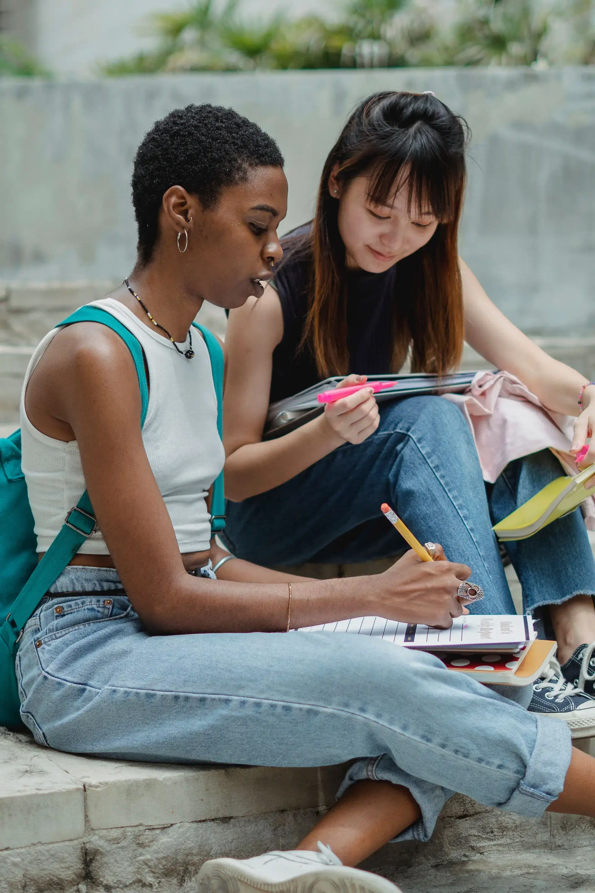 Two young women sitting on steps, working through a workbook together